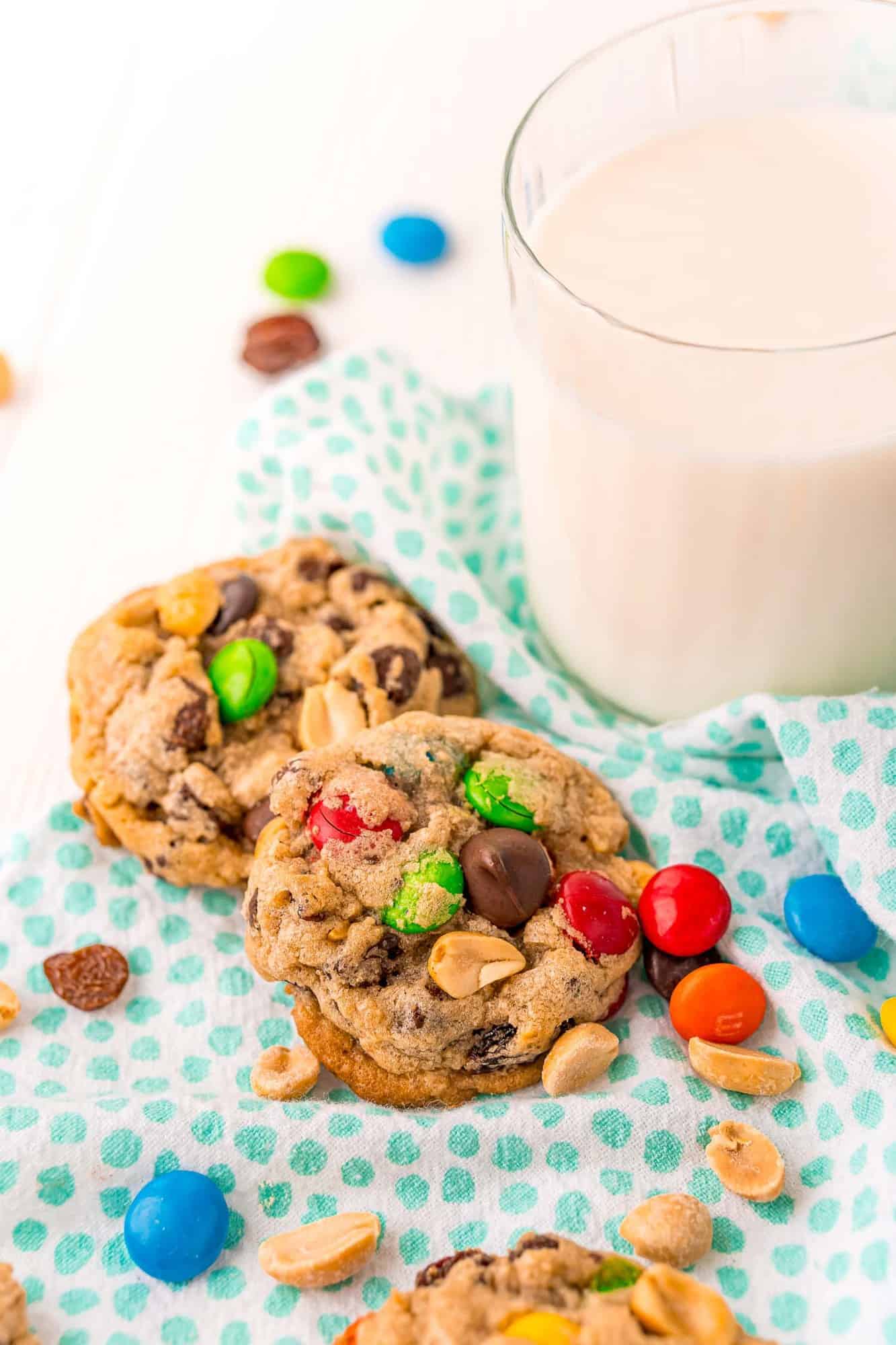 Two trail mix cookies by a glass of milk.