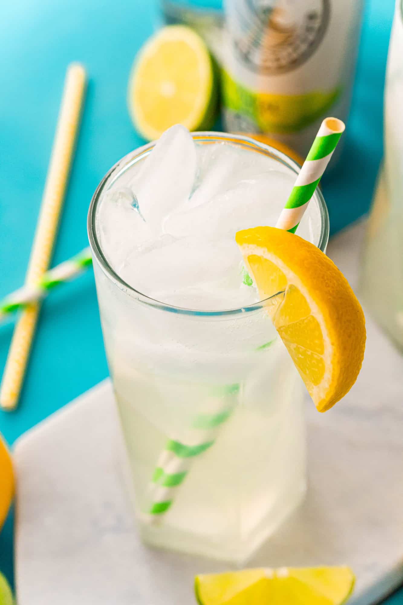 Glasses of iced beverage with a green and white paper straw and an orange wedge.