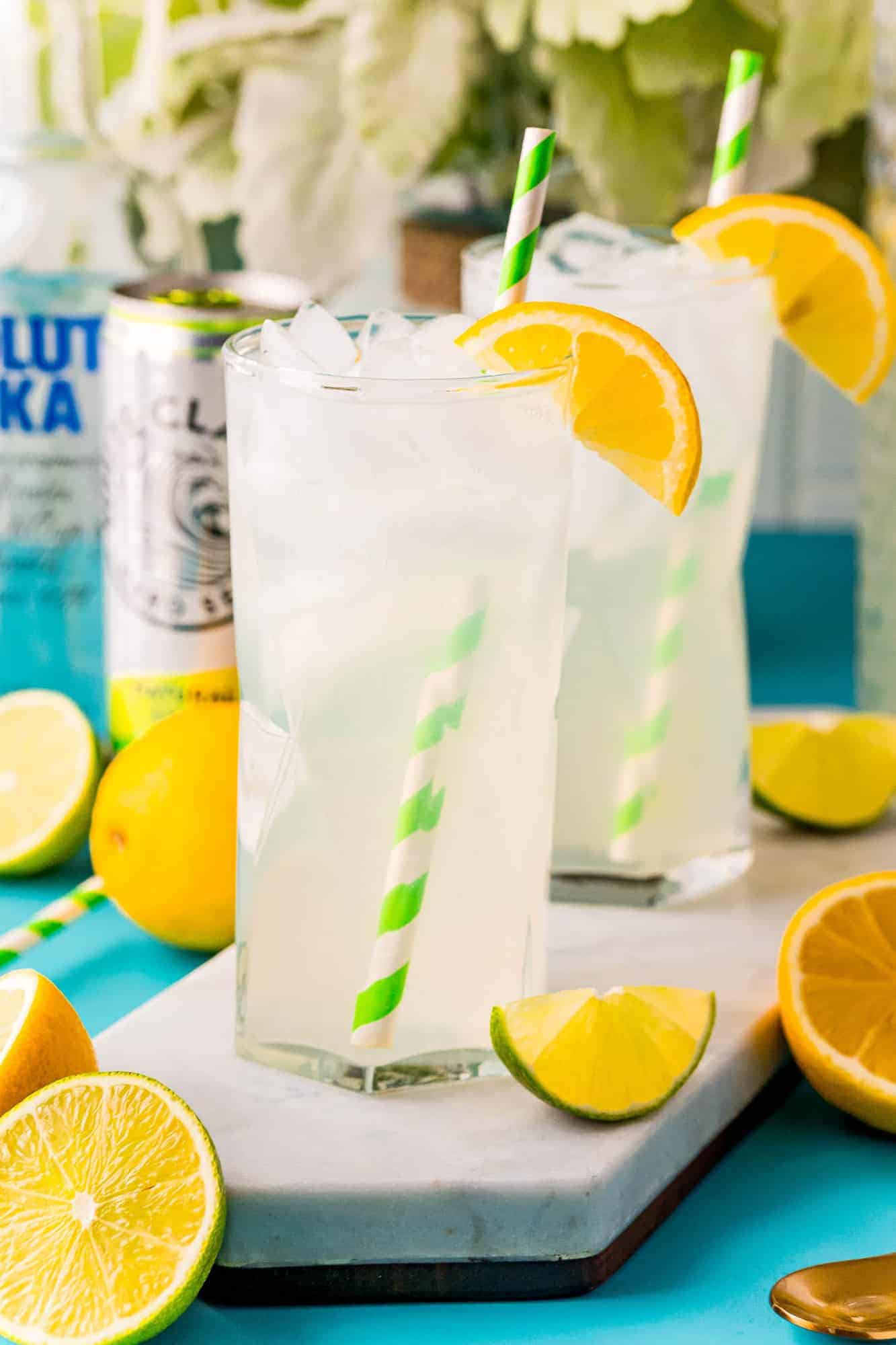 Two tall glasses of lemonade with green and white straws, a can of white claw in the background.