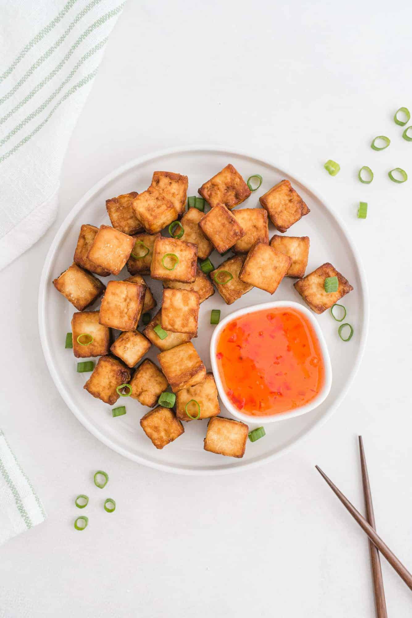 Cooked tofu on a plate with sweet chili sauce and green onions.