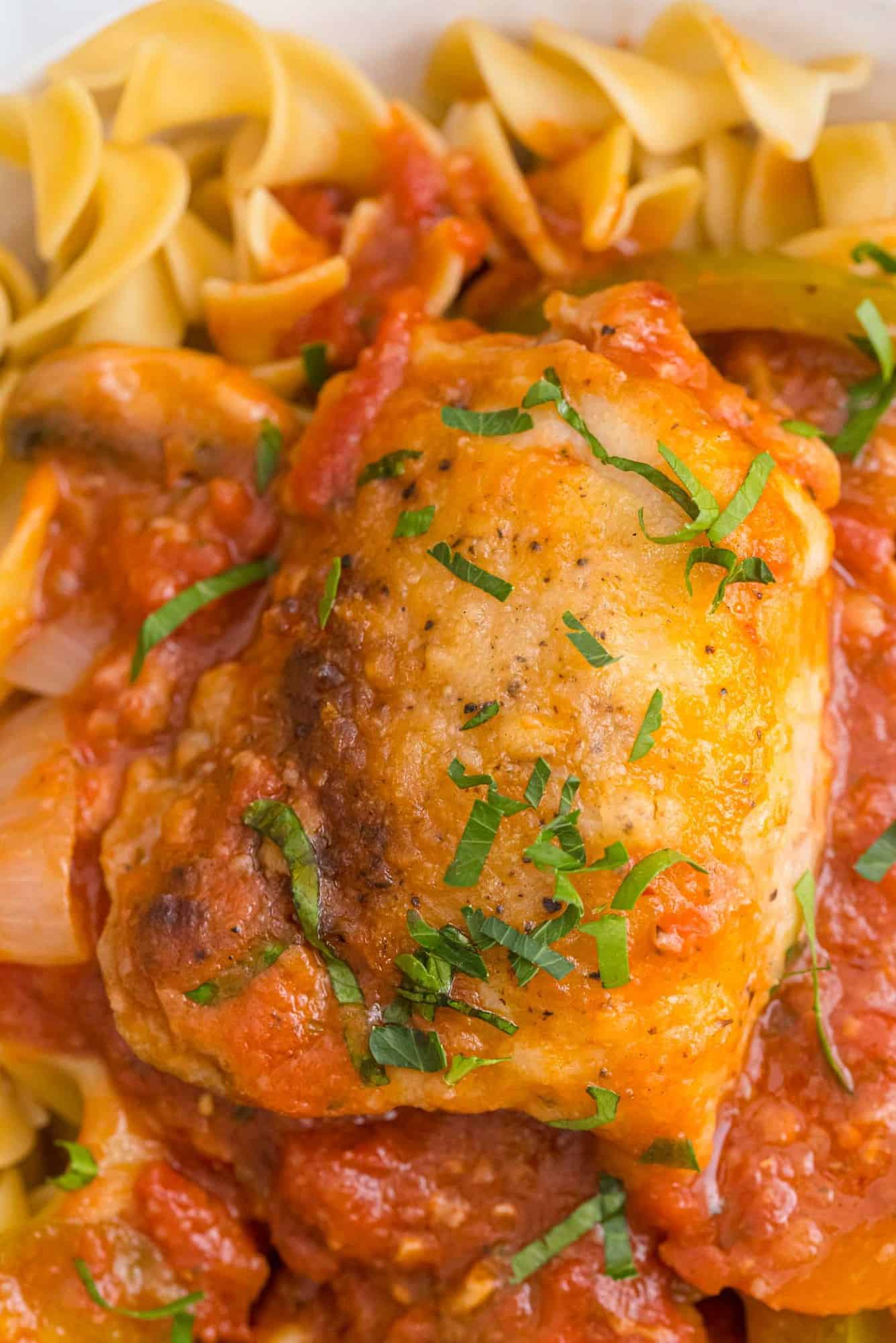 Chicken cacciatore served on top of curly egg noodles, garnished with parsley.