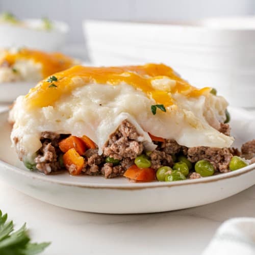 Slice of shepherd's pie on a white plate with a baking dish in the background.