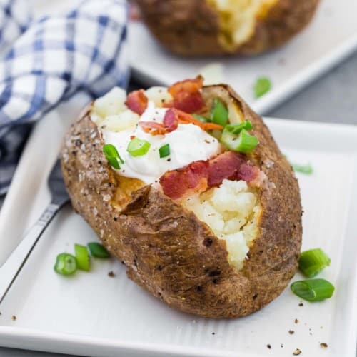 A potato split open and topped with sour cream, bacon, and green onions.