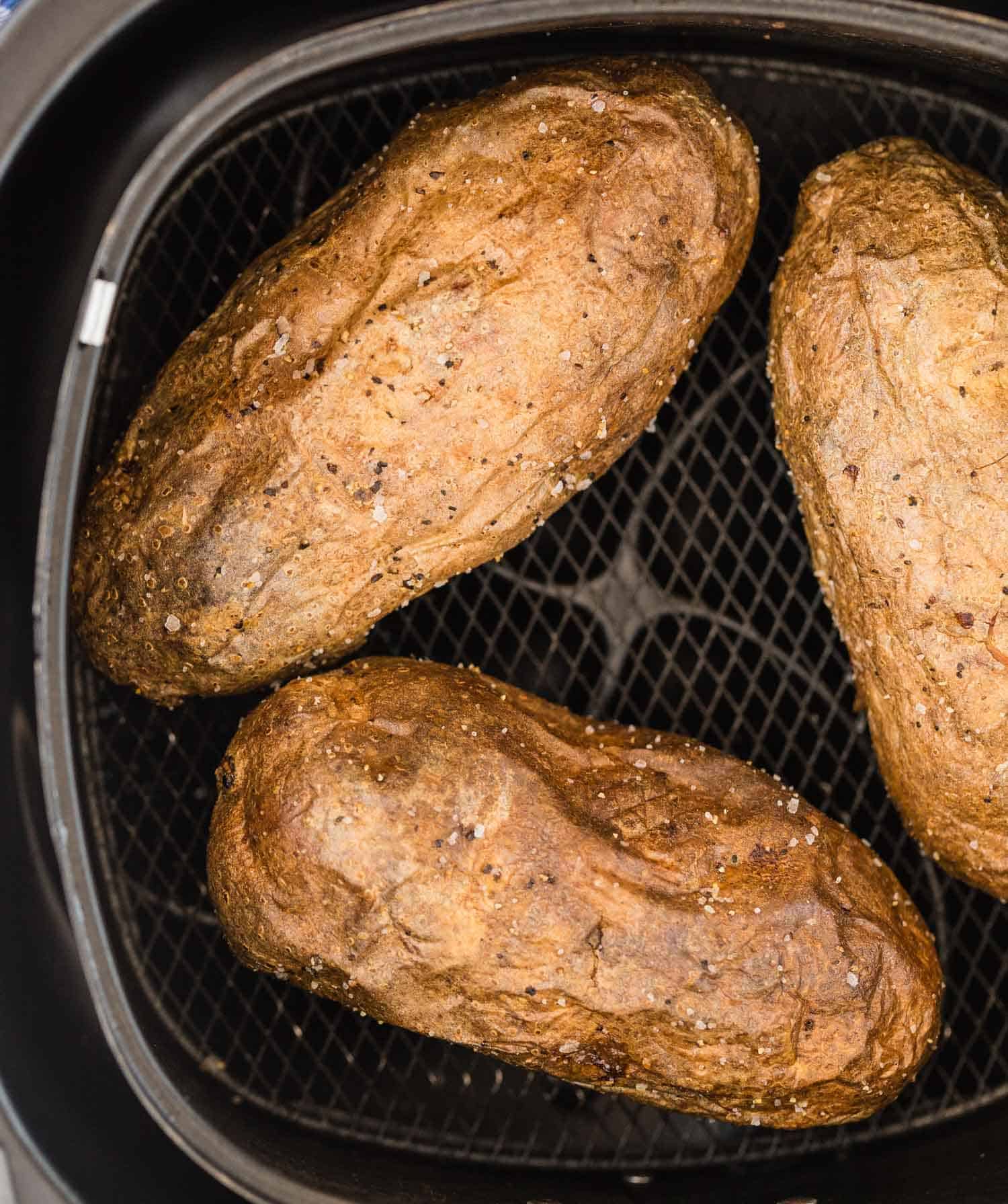 Close up of baked potatoes in an air fryer basket.