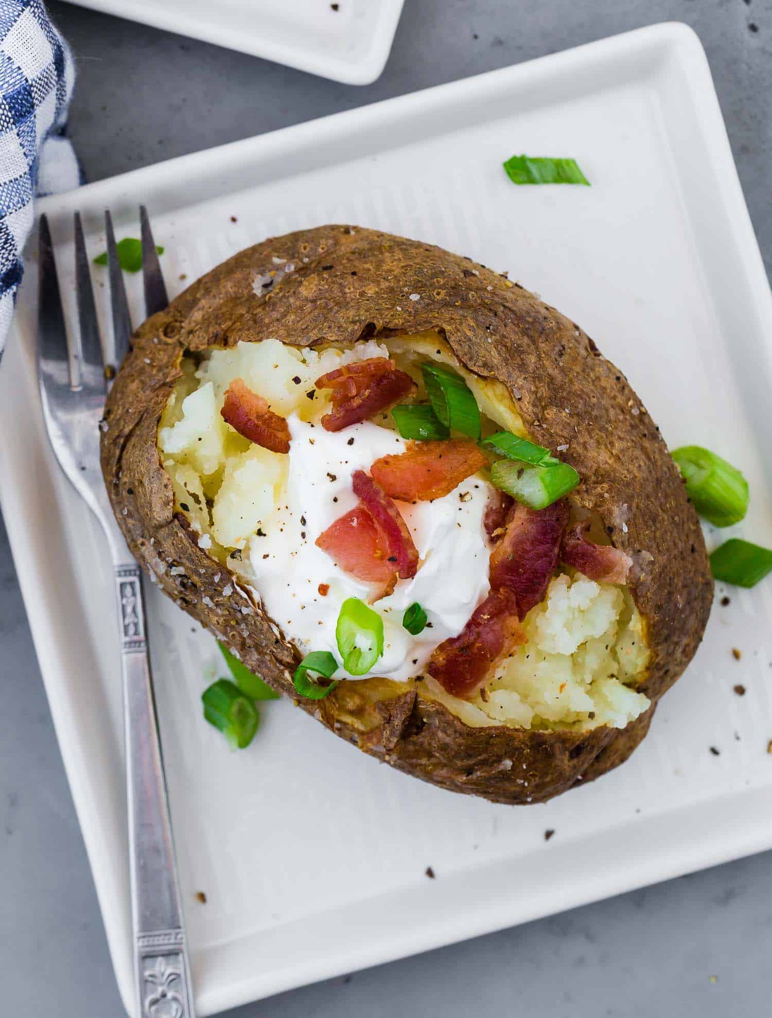 Overhead view of a baked potato with sour cream, green onions, and bacon.