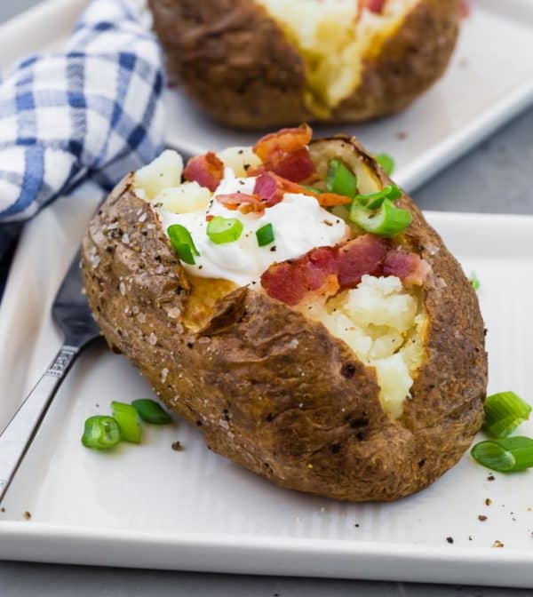 Potato with toppings on a square white plate.