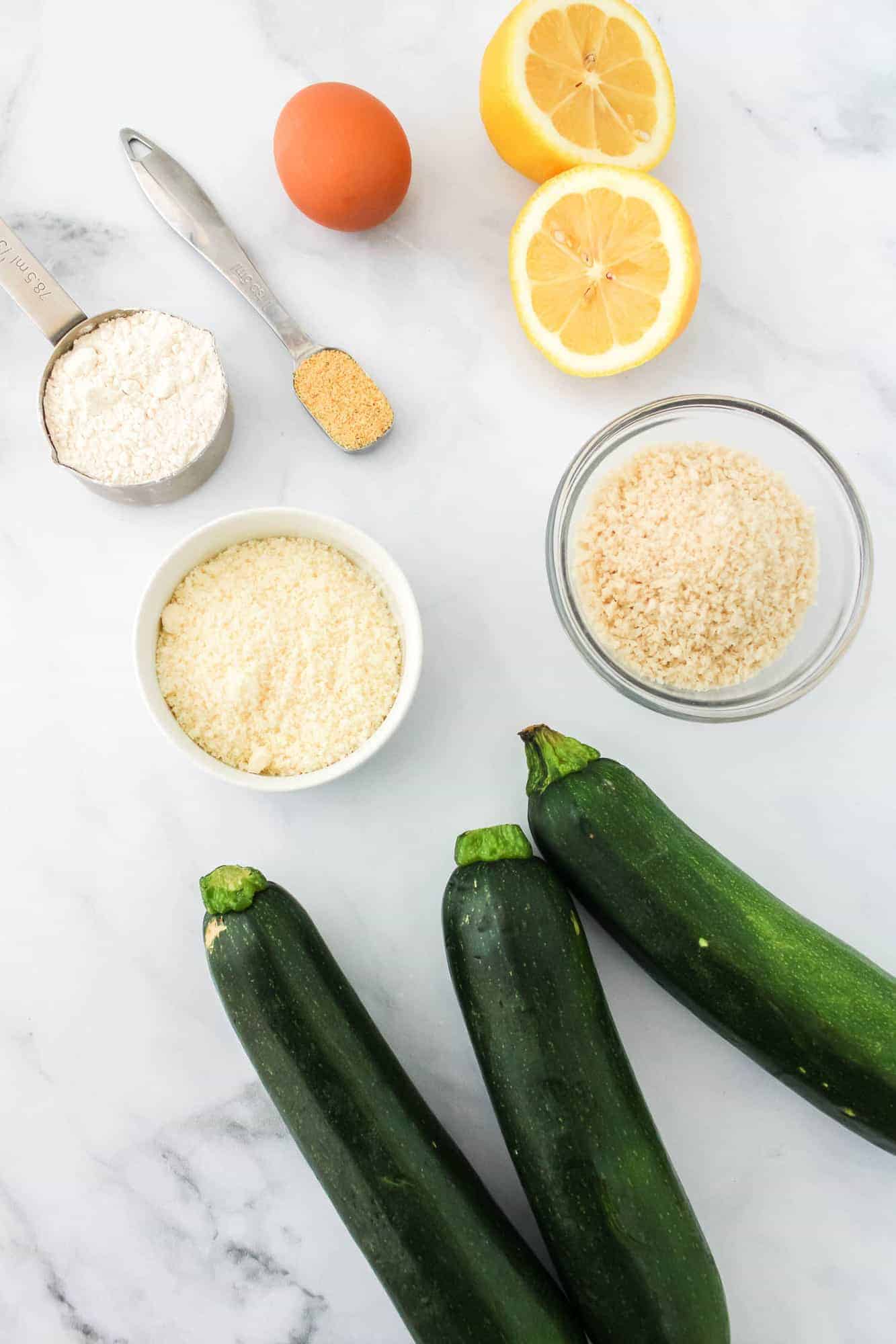 Overhead view of zucchini, breading ingredients, and a lemon half.