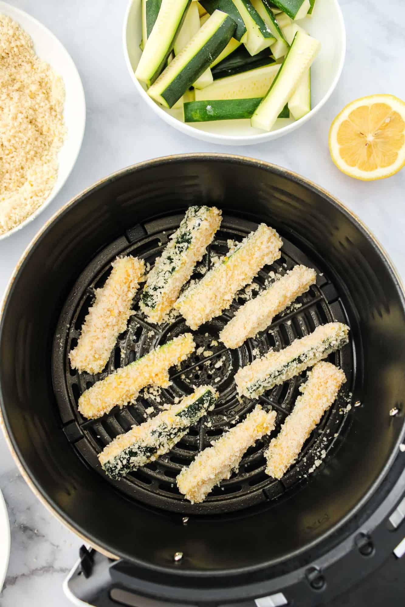 Breaded uncooked zucchini fries in an air fryer basket.