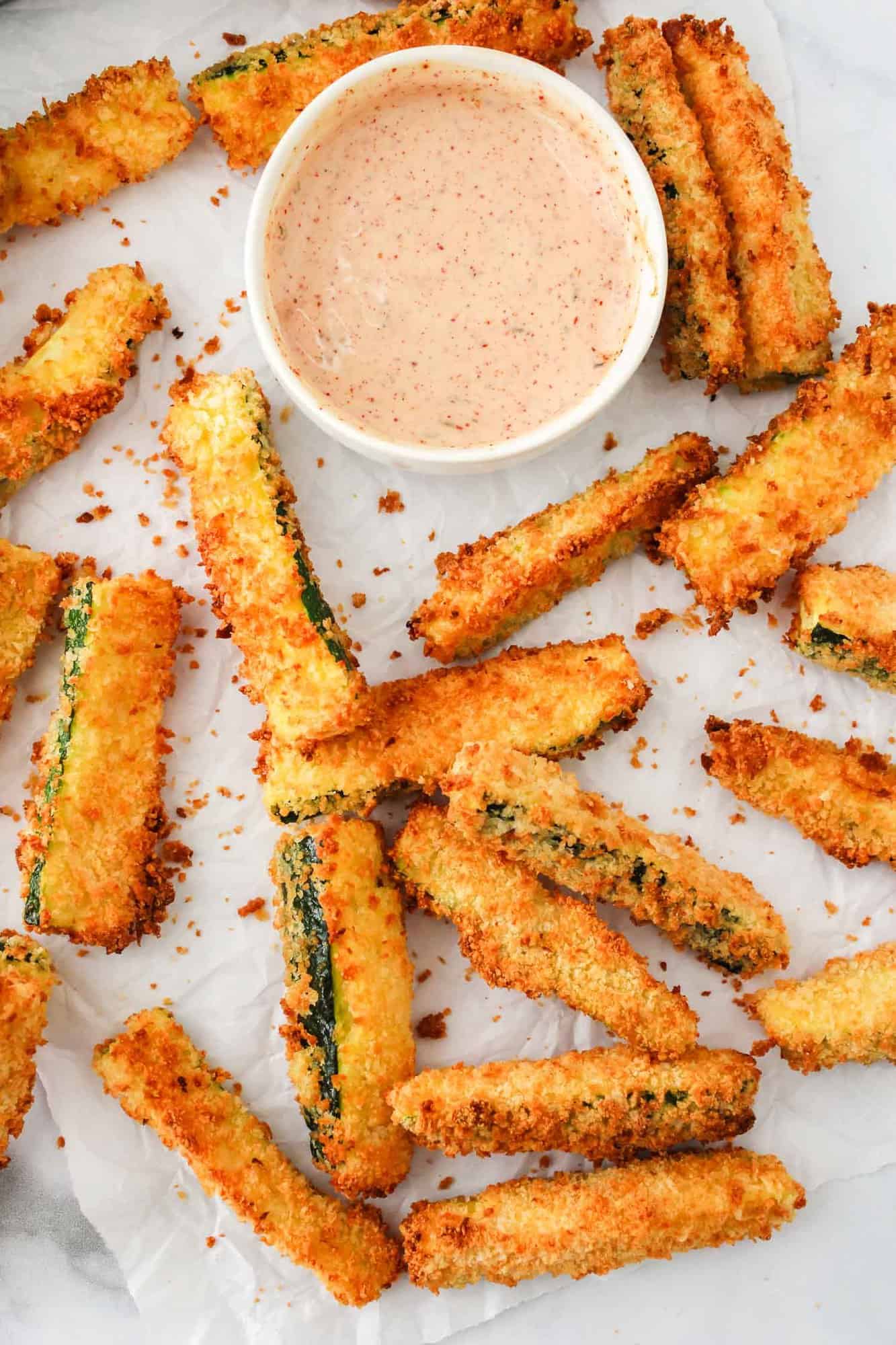 Air fryer zucchini fries on parchment with a light red dipping sauce.