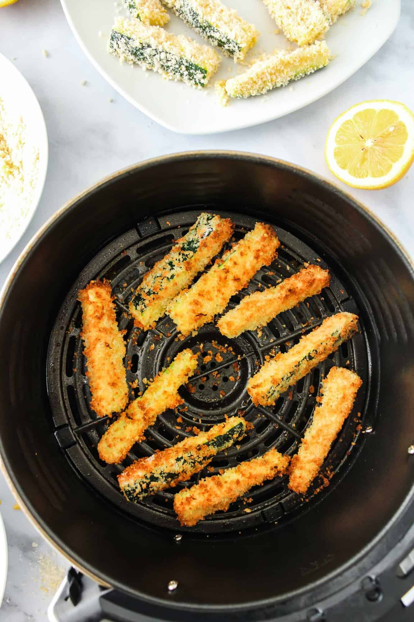 Cooked zucchini fries in an air fryer basket.