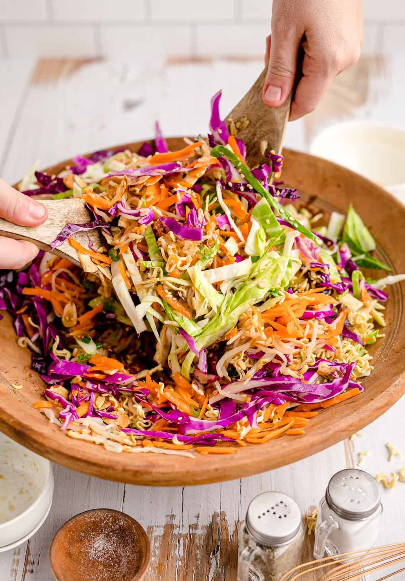 Large salad in a wooden bowl being tossed with handheld salad tongs.