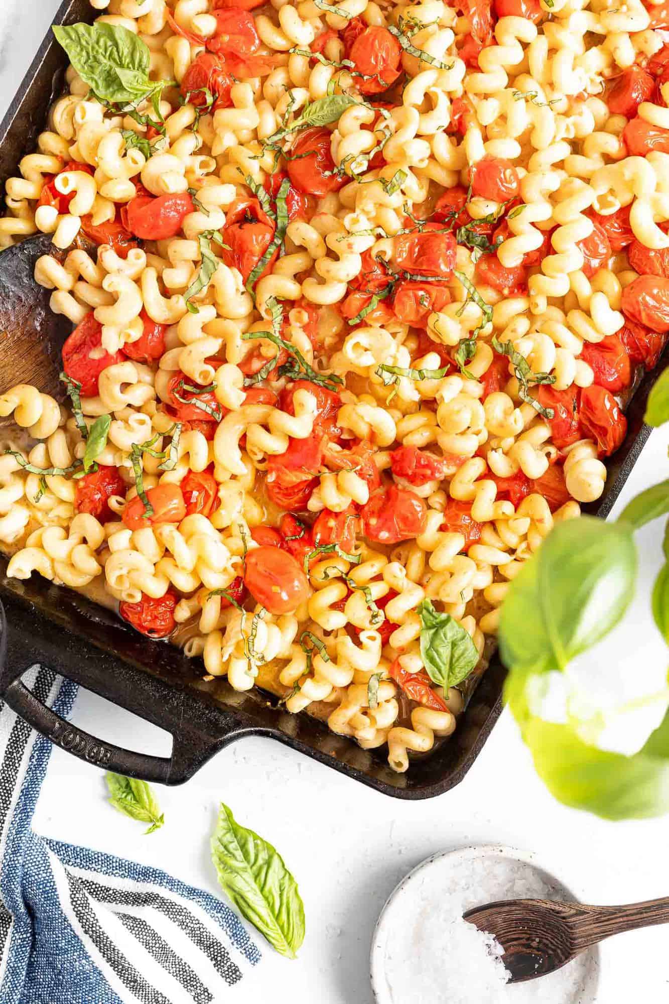 Black baking dish filled with pasta, tomatoes, and basil.