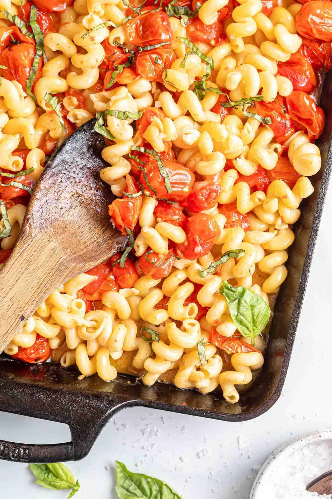 Pasta with tomatoes, basil, and feta cheese in a black baking dish.