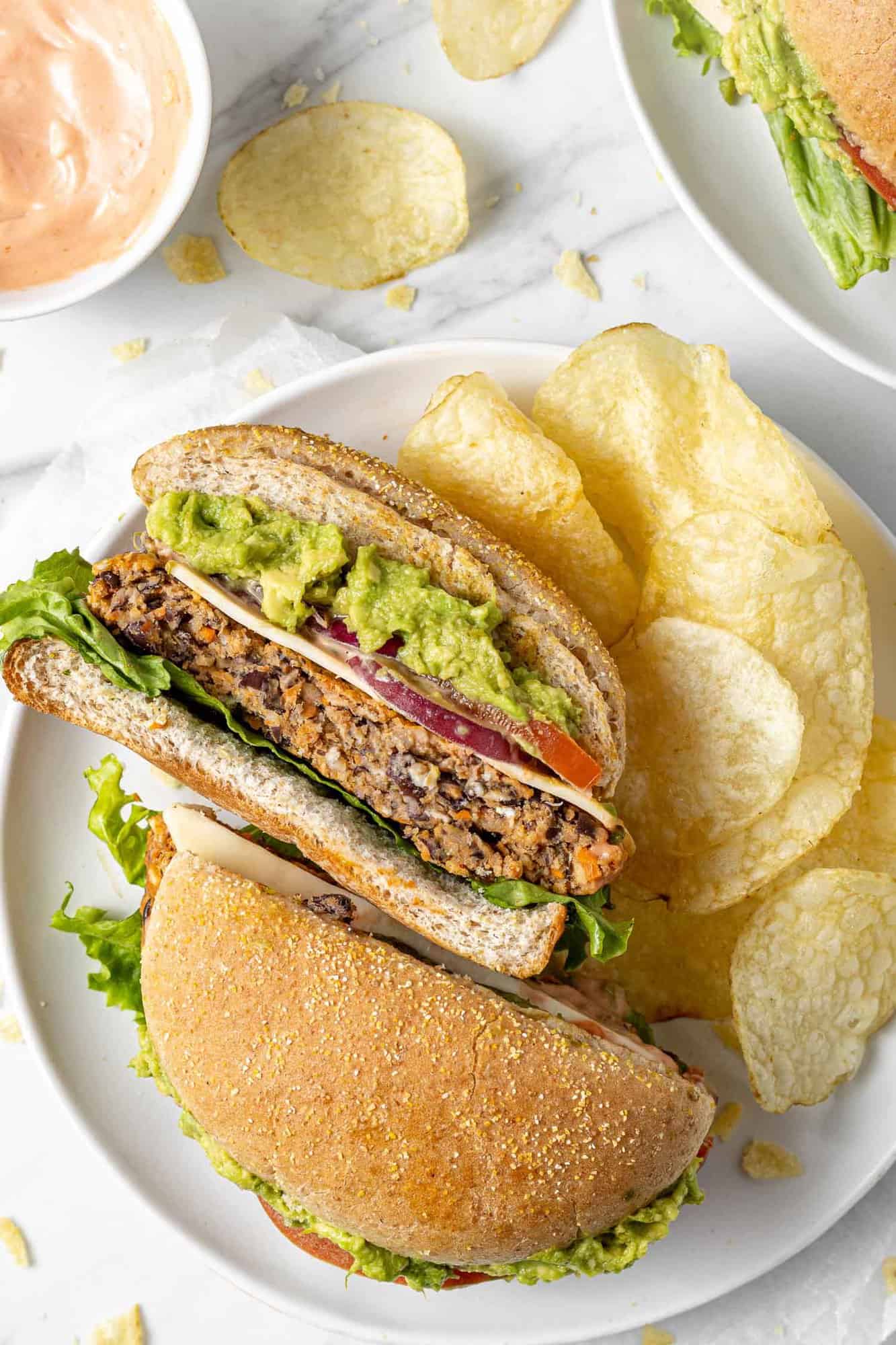 A bean burger cut in half on a plate with potato chips.