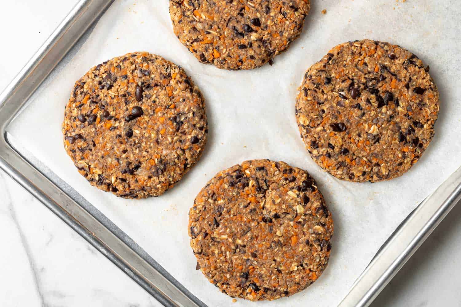 Bean burgers on a parchment paper lined baking sheet.