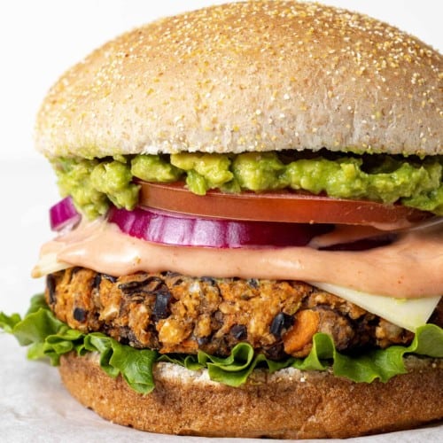 Black bean burger on a whole wheat bun with lots of toppings including guacamole, onion, tomato, and lettuce.