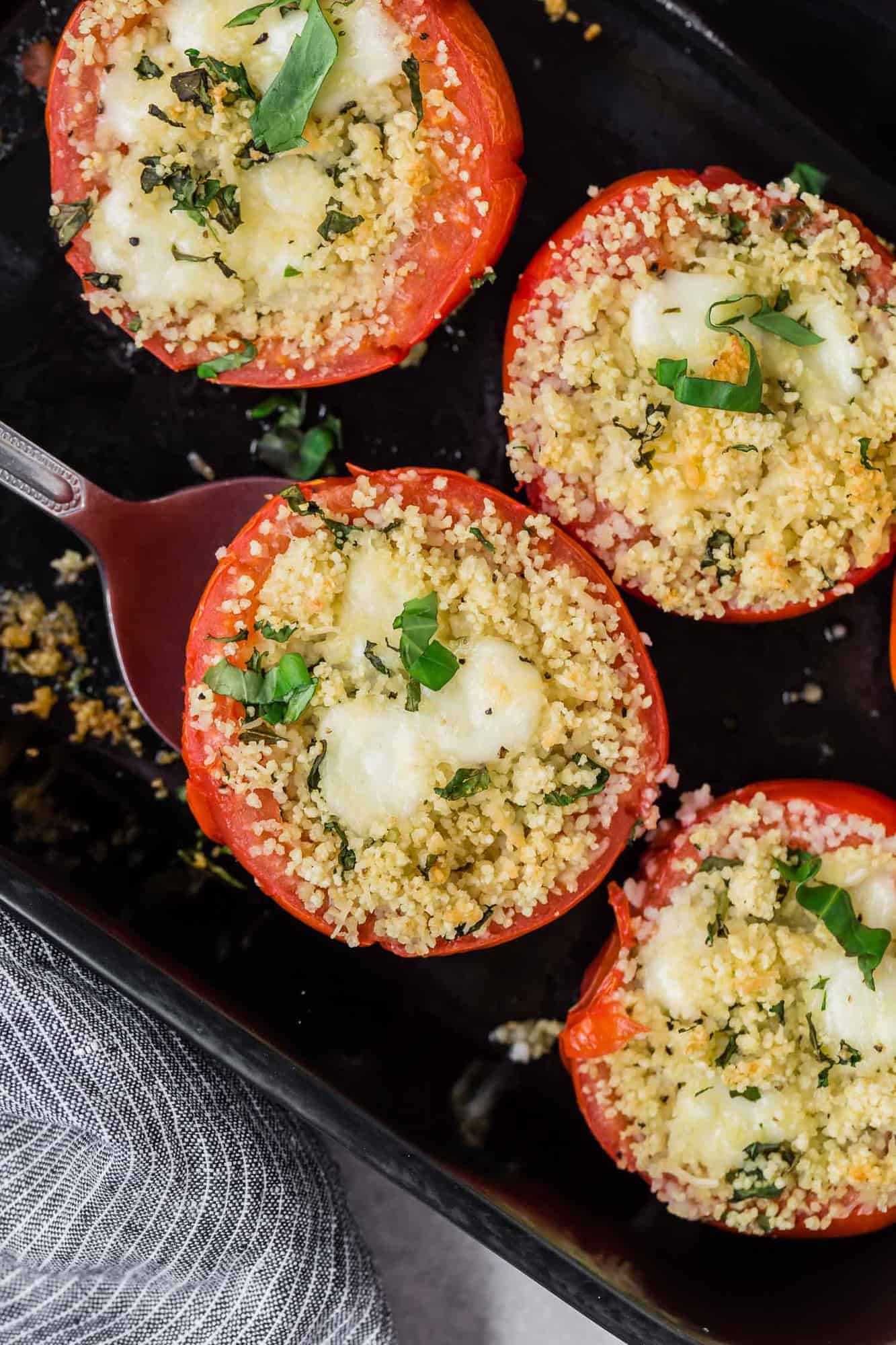 Overhead view of caprese stuffed tomatoes, one with a spatula under it.