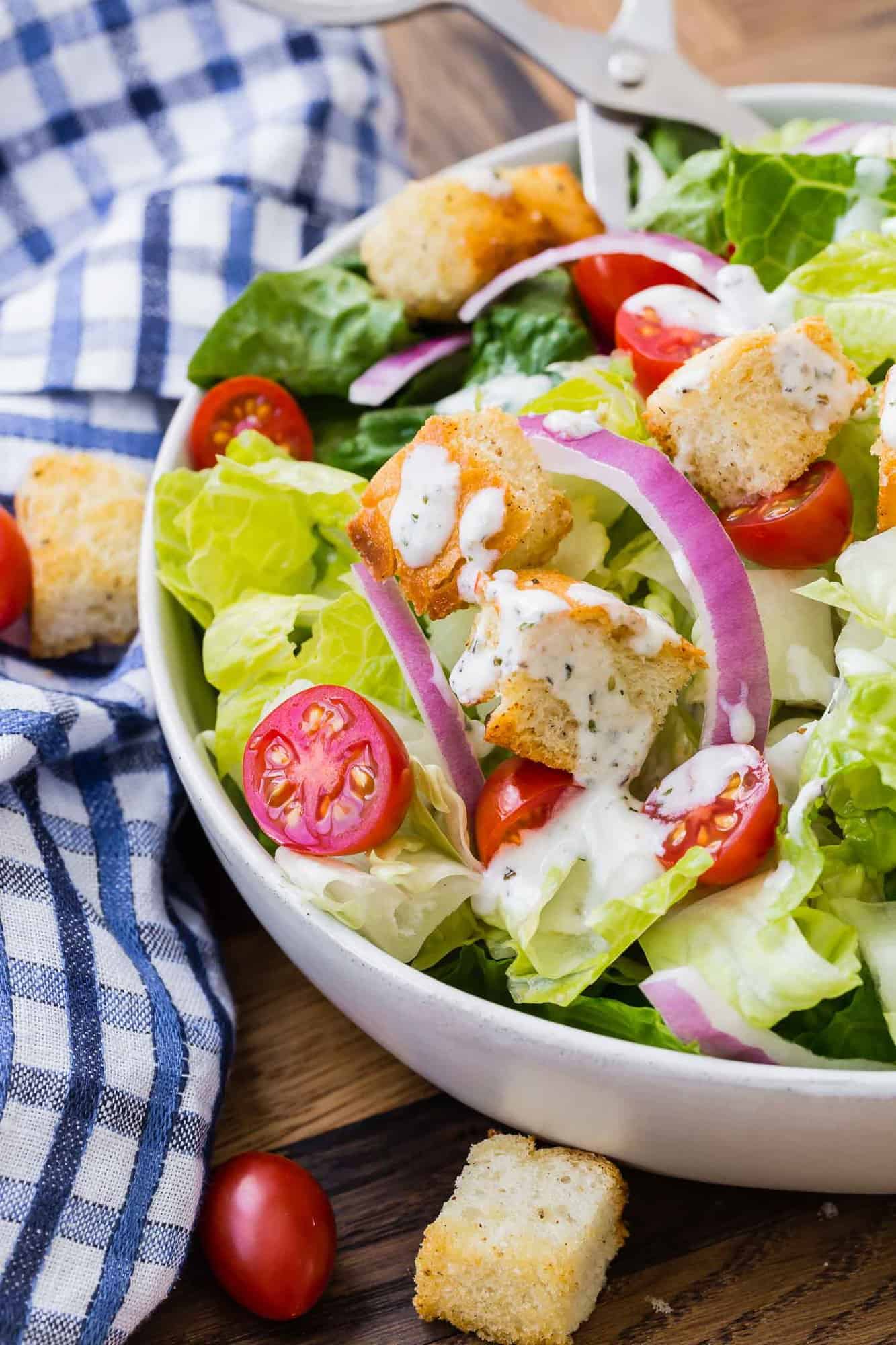 Close up of salad with croutons, red onions, tomatoes, and a creamy italian dressing.