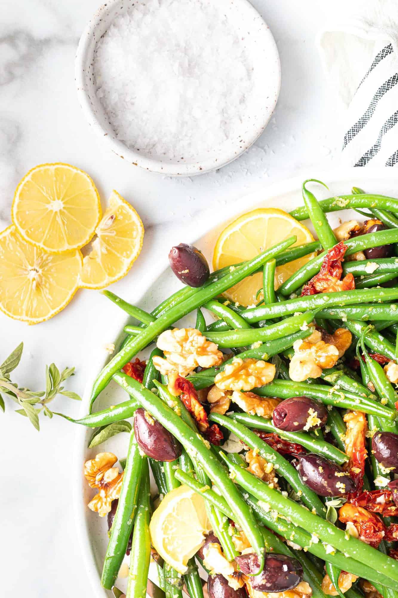 Colorful green bean salad, lemon slices and salt nearby.