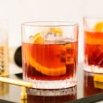 Dark red cocktail with ice and an orange slice.