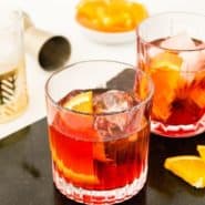 Dark red cocktail with an orange in it, text overlay reads "how to make the perfect negroni, rachelcooks.com"