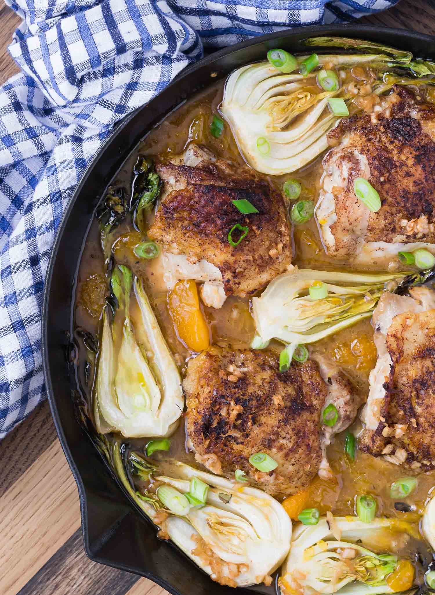 Overhead view of a skillet with chicken thighs, bok choy, and oranges.