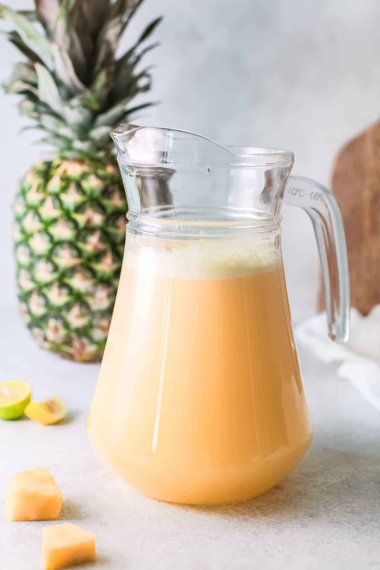 Pineapple water in a pitcher, with a large pineapple in the background.