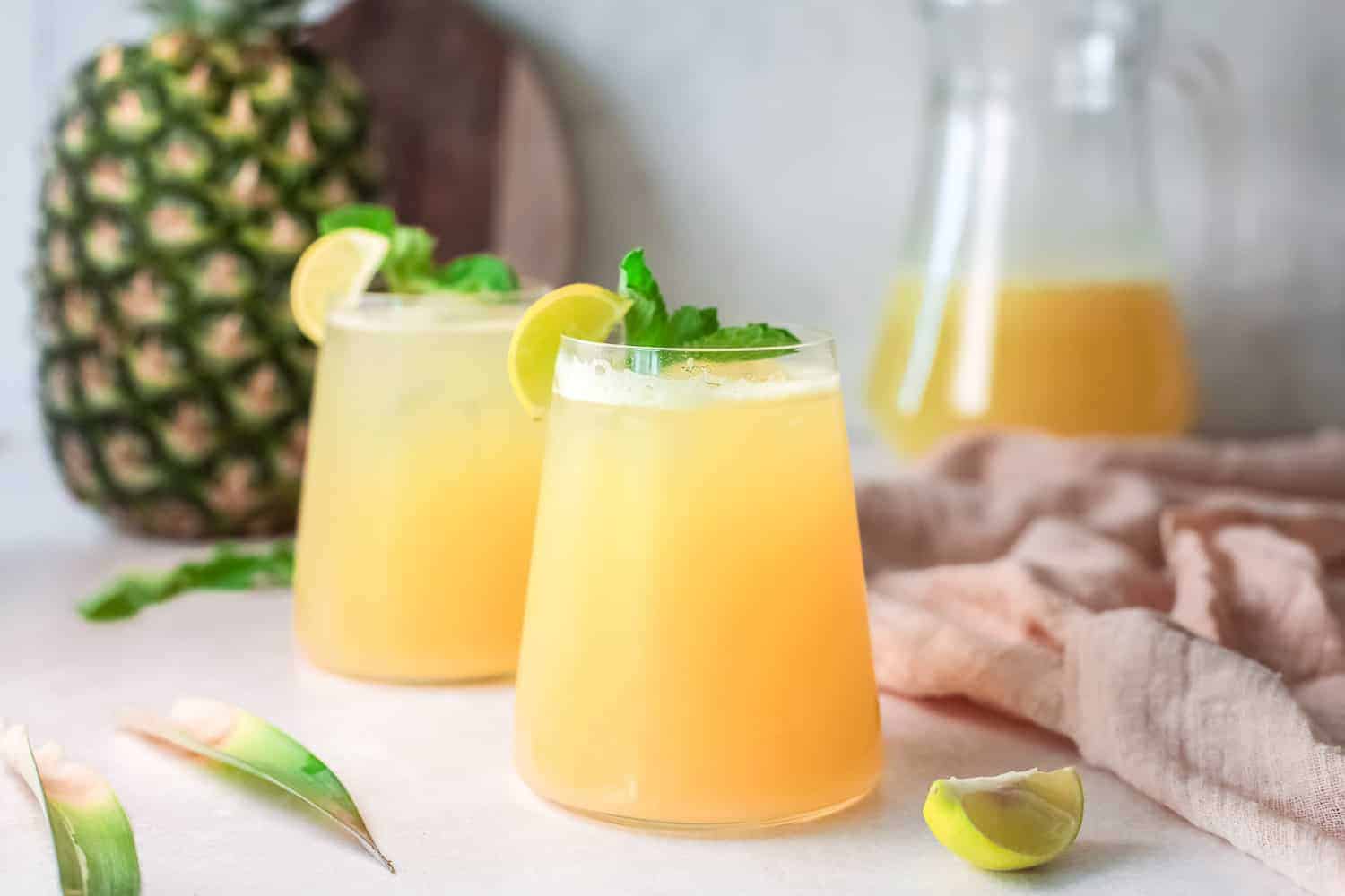 Two glass of light yellow water made with pineapple, garnished with fresh mint and lime.