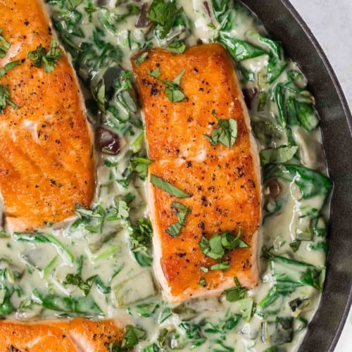 Overhead view of seared salmon settled in a bed of a spinach cream sauce.