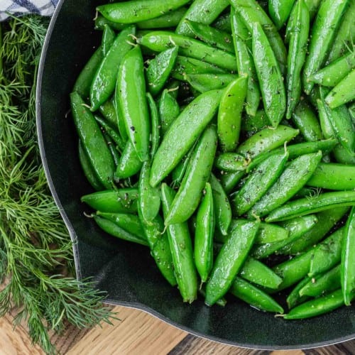 Bright green sugar snap peas in a black skillet, garnished with fresh dill.