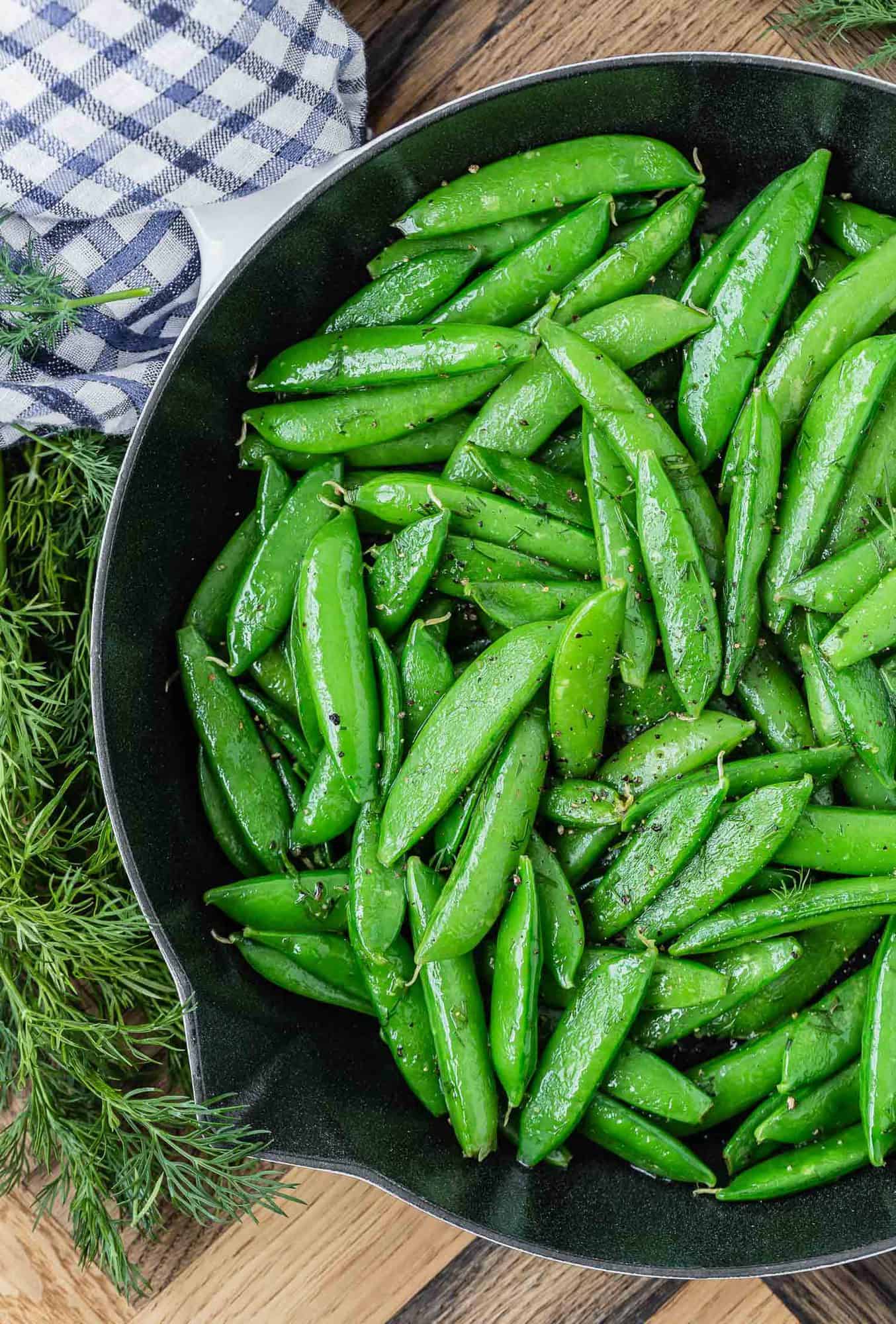 Cast iron pan with cooked sugar snap peas and fresh dill.