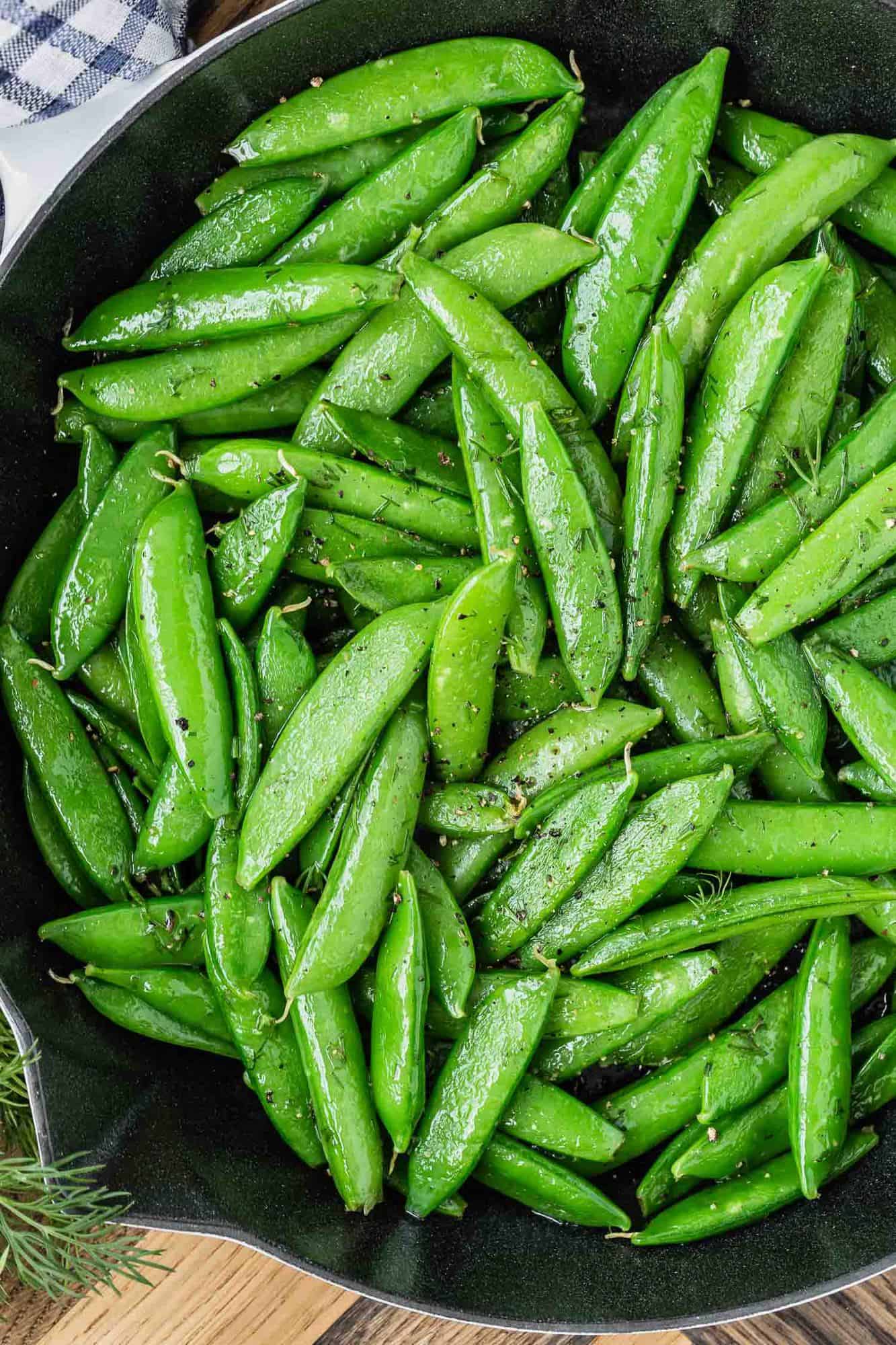 Close up of cooked snap peas in a black skillet.