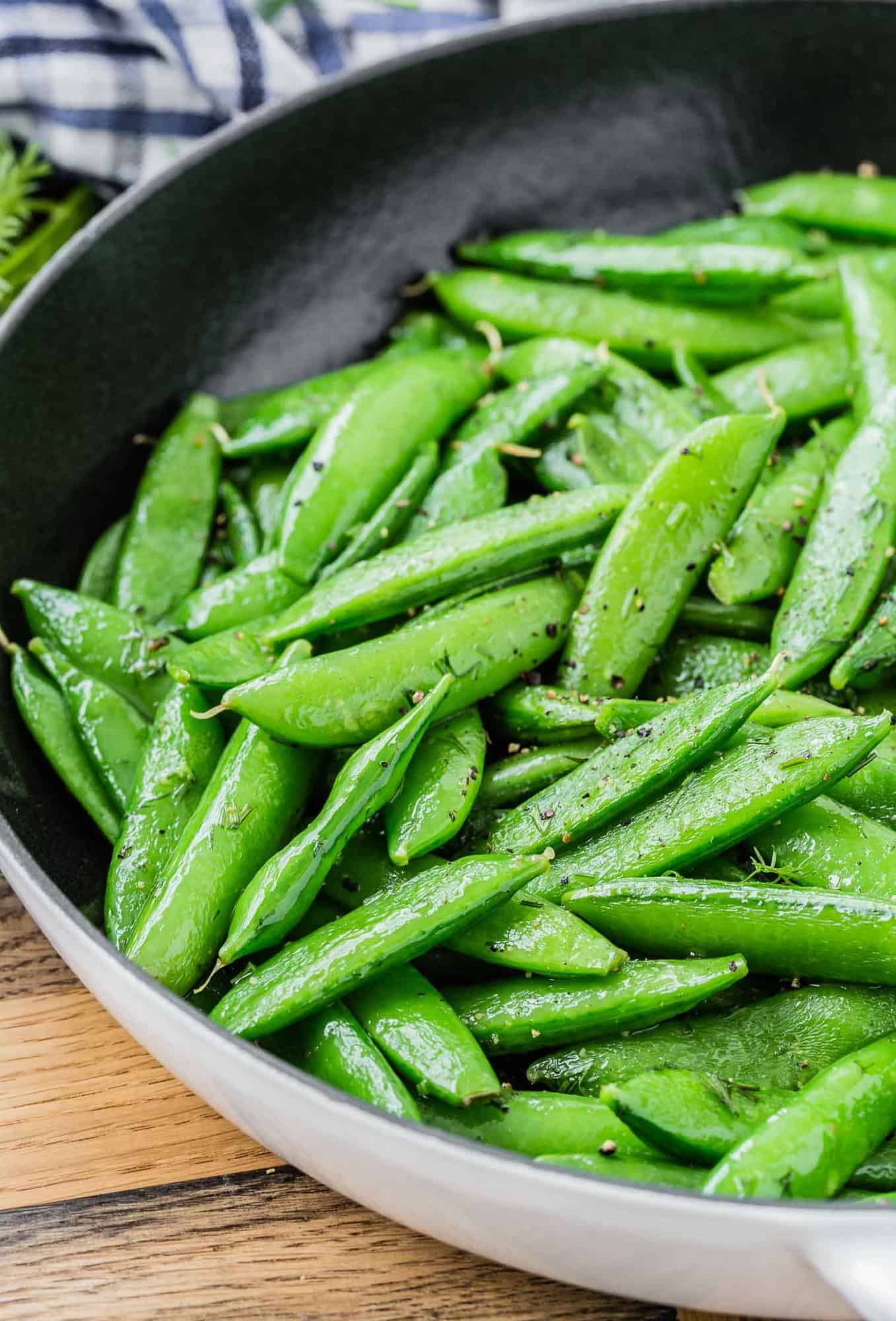 Sugar snap peas in a black and white skillet on a wooden surface.