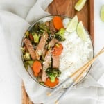 A bowl filled with rice, beef, vegetables, and topped with sesame seeds. Chopsticks also visible.