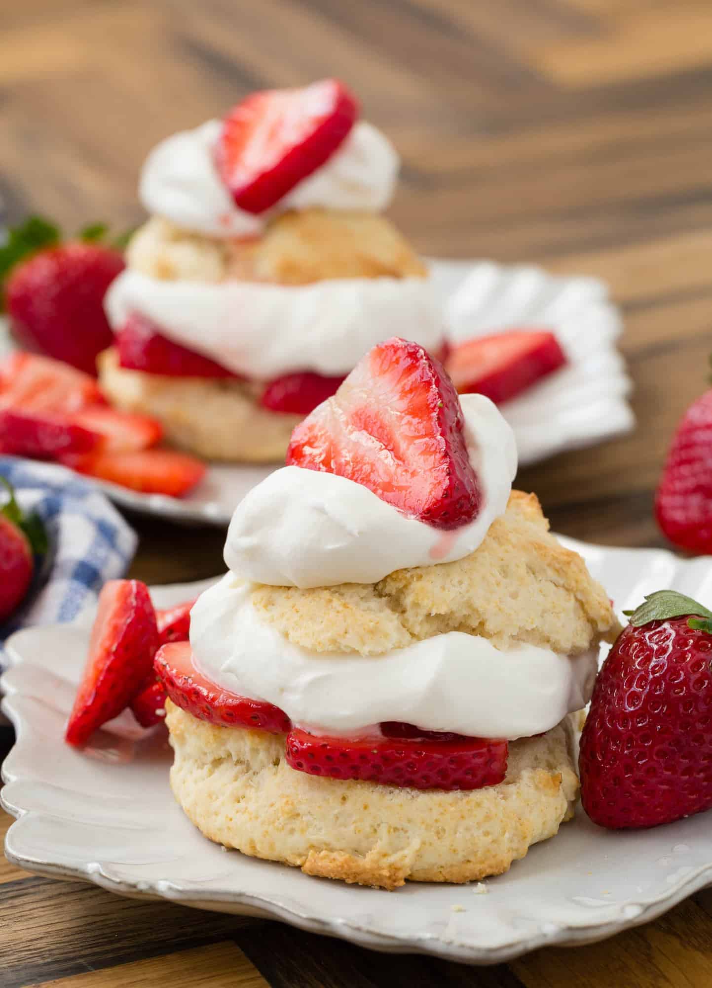 Decorative white plate with strawberry shortcake on it, topped with whipped cream and strawberries.