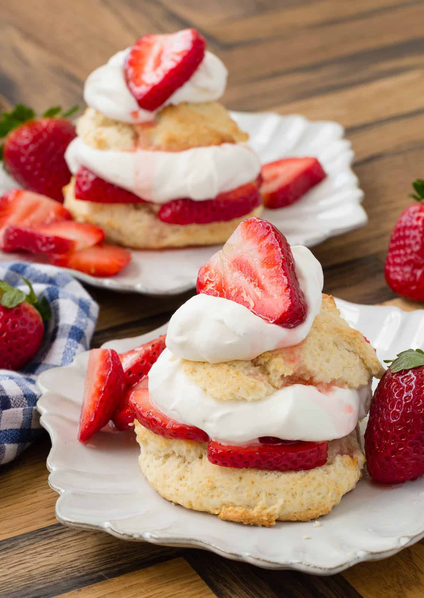 Two white plates with strawberry shortcakes with whipped cream.