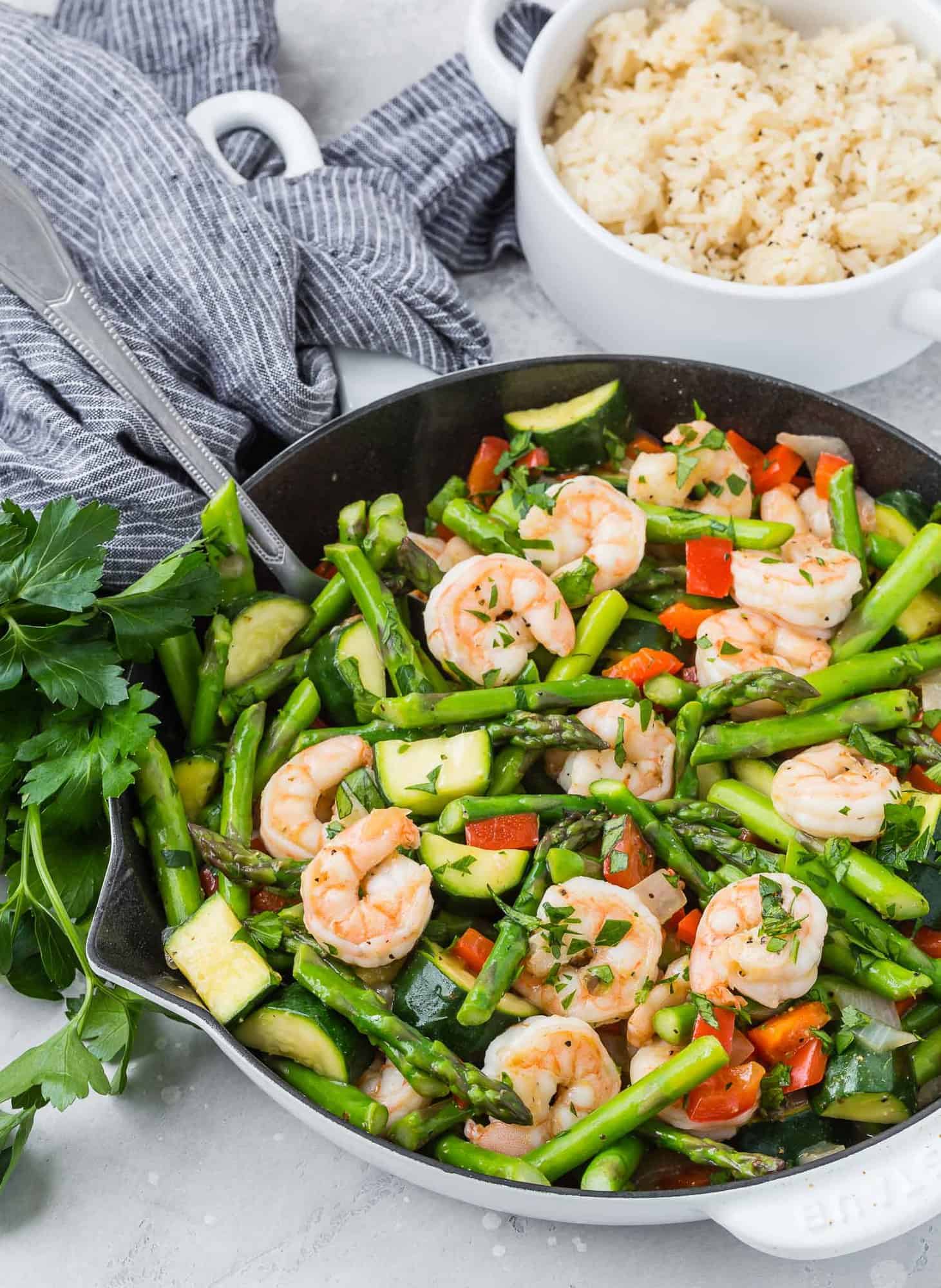 Shrimp stir fry in a white skillet, cooked rice in the background.