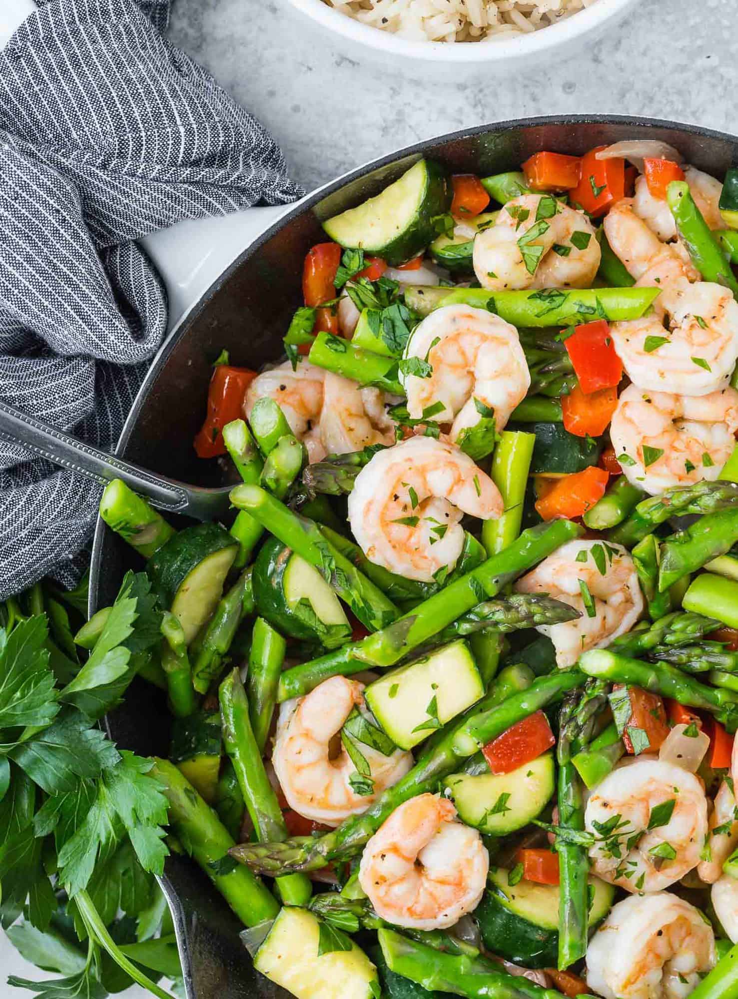 Cooked shrimp and vegetables in a skillet with a black and white linen nearby.