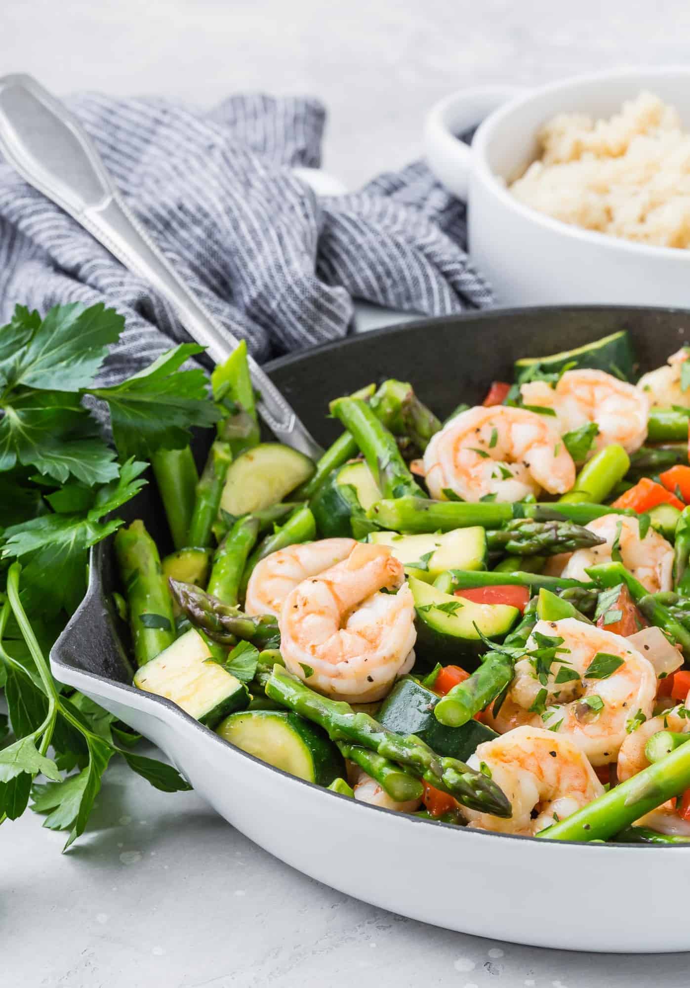 Stir fry with shrimp and asparagus in a white skillet with a silver spoon.