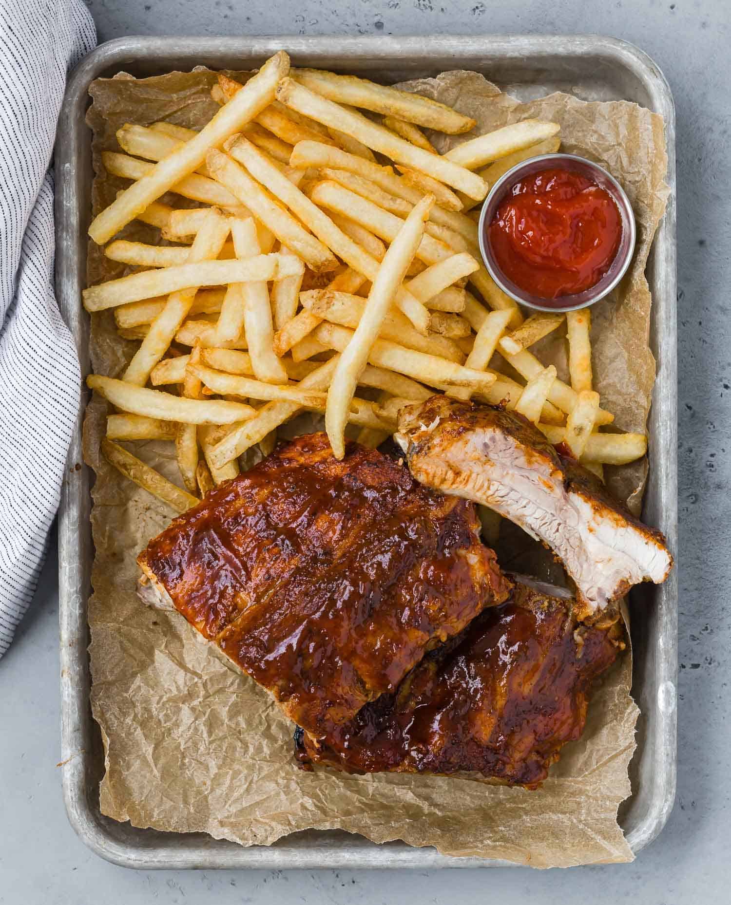 Overhead view of ribs on a tray with fries and ketchup.