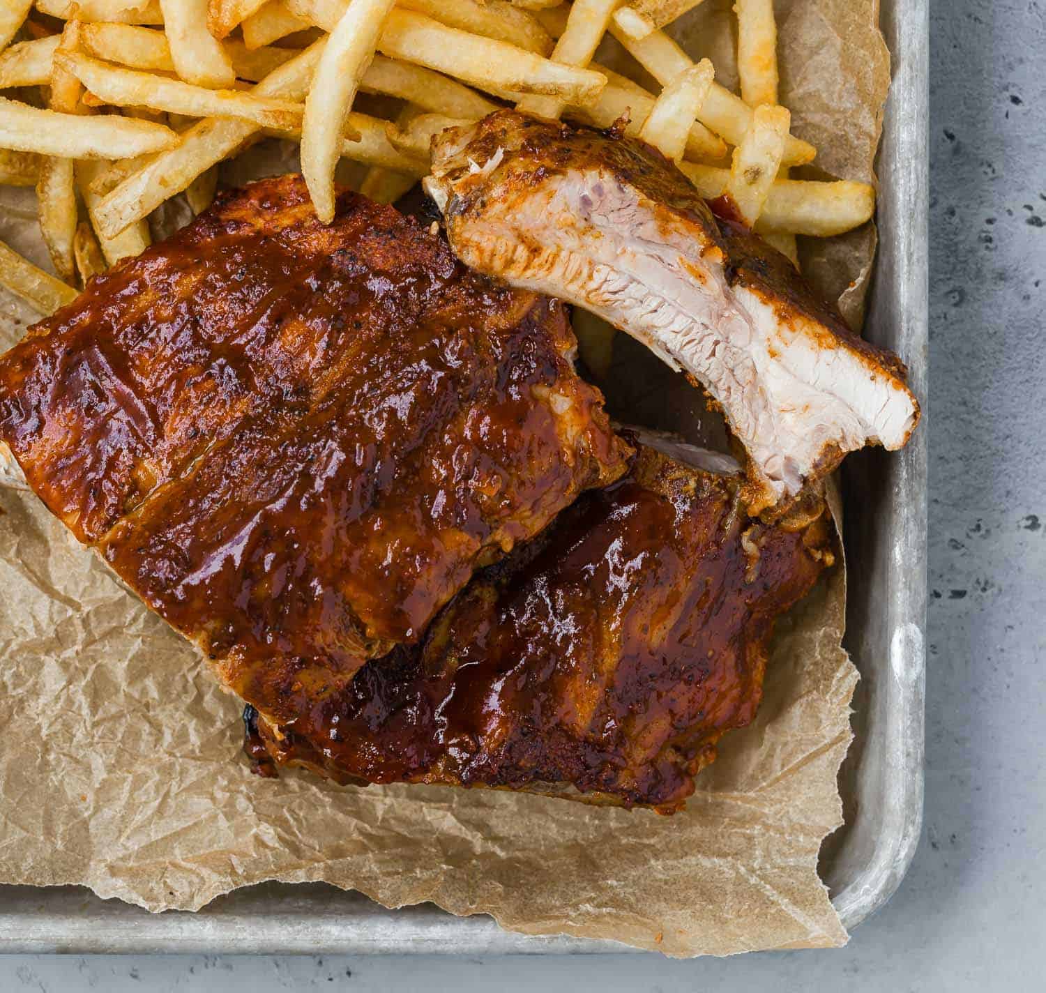 A tray lined with brown parchment, topped with bbq ribs and french fries.