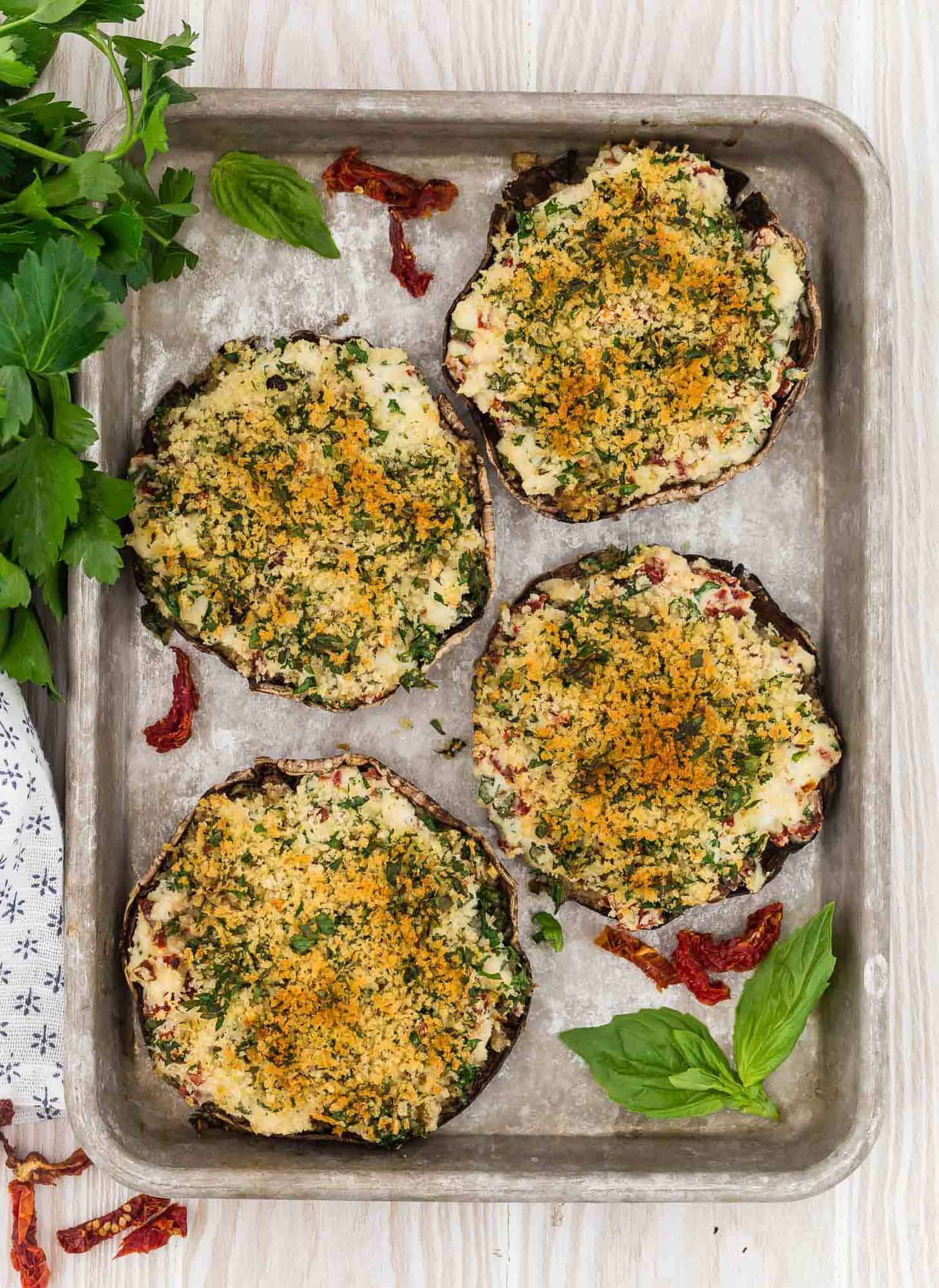 Overhead view of 4 portobello mushrooms on a baking sheet, filled with stuffing and baked.