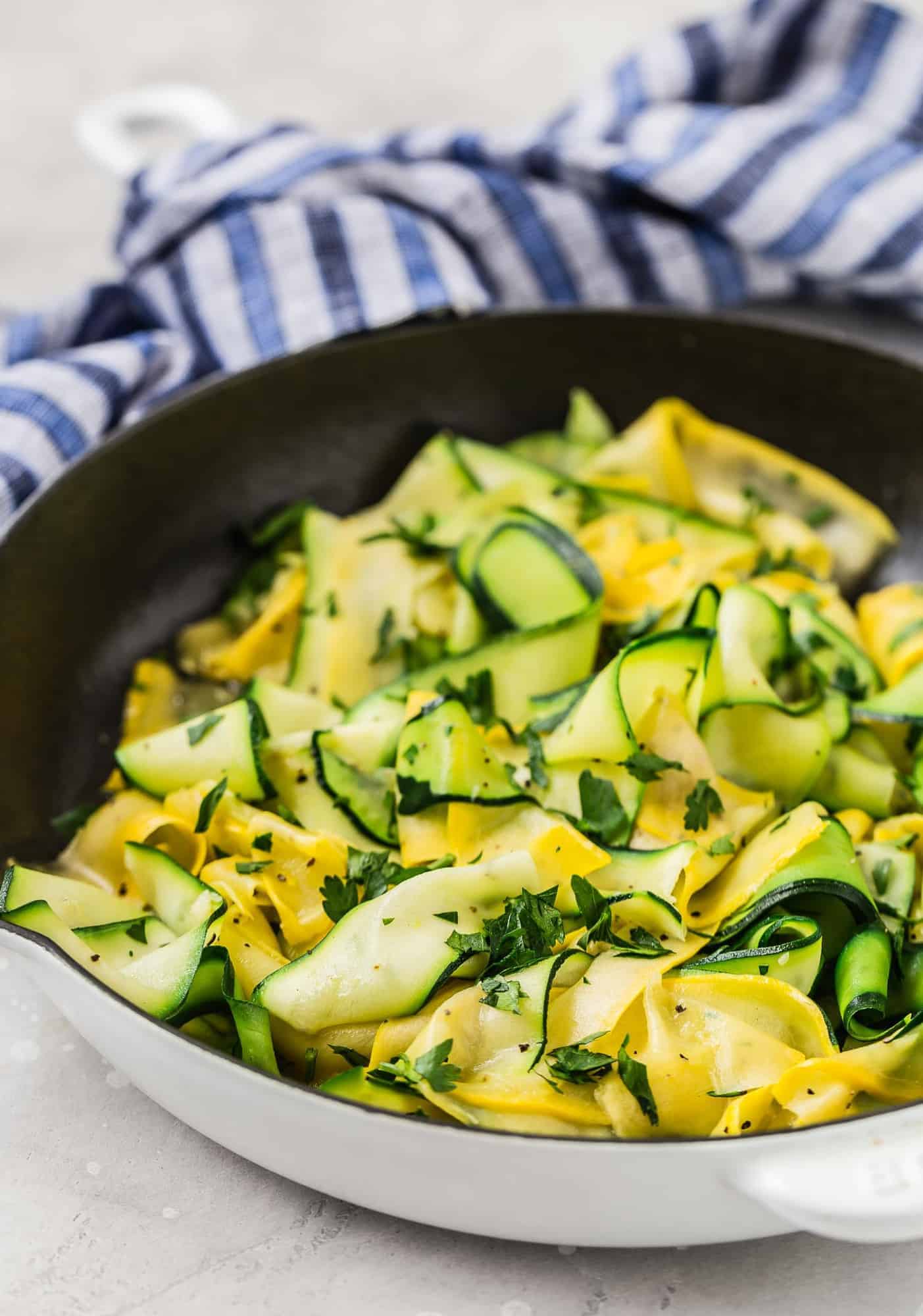 Summer squash and zucchini ribbons in a black and white skillet with a blue and white linen.