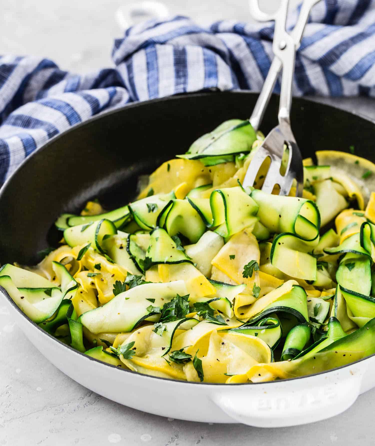 Ribbons of zucchini and summer squash in a frying pan with tongs.