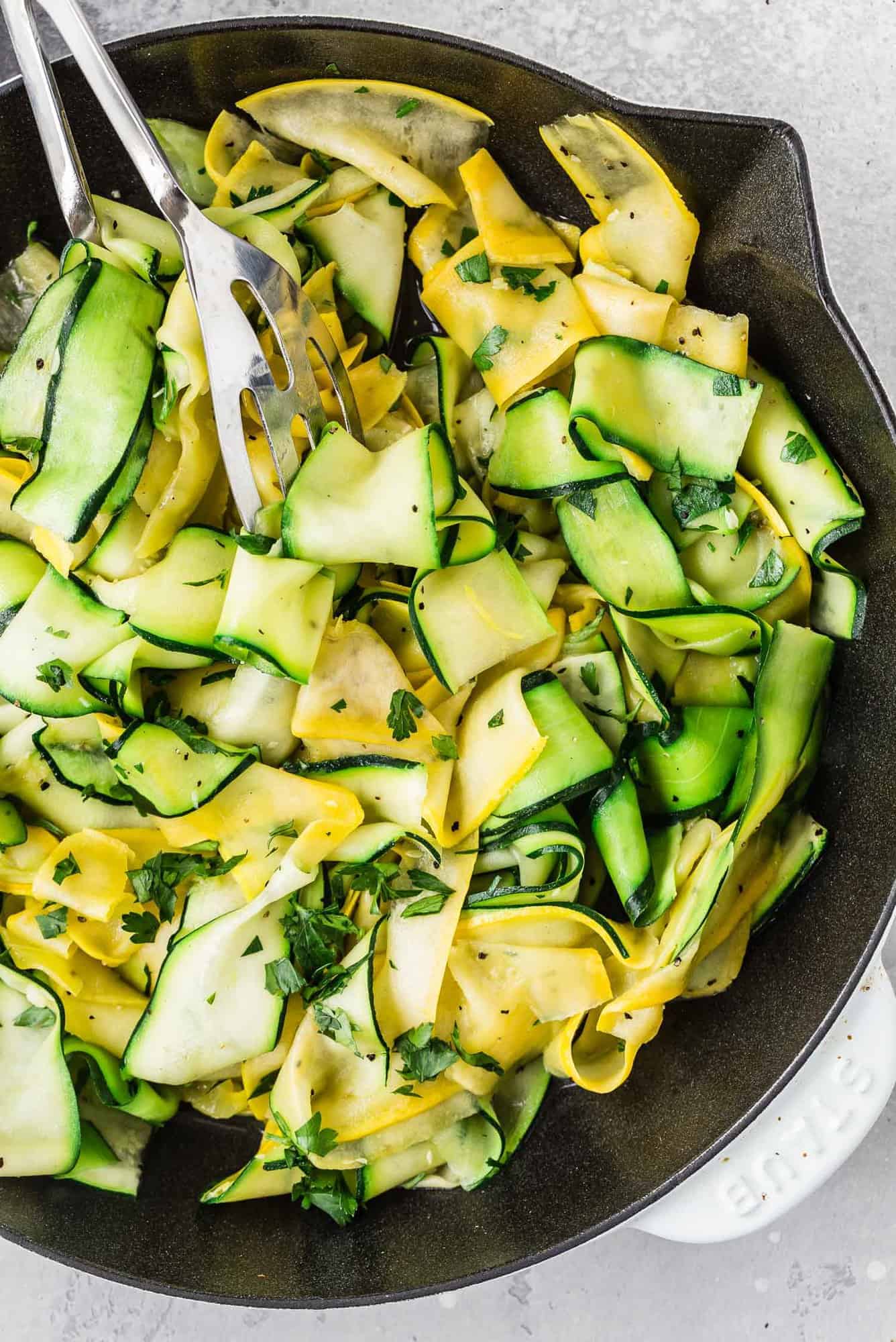 Zucchini and summer squash ribbons in a white and black skillet.