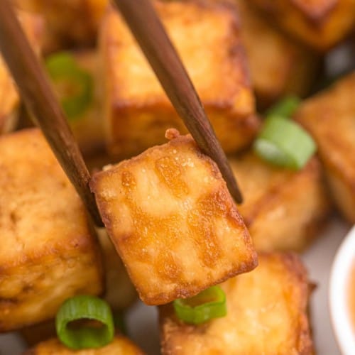 Pile of crispy air fryer tofu, one piece between two chopsticks.