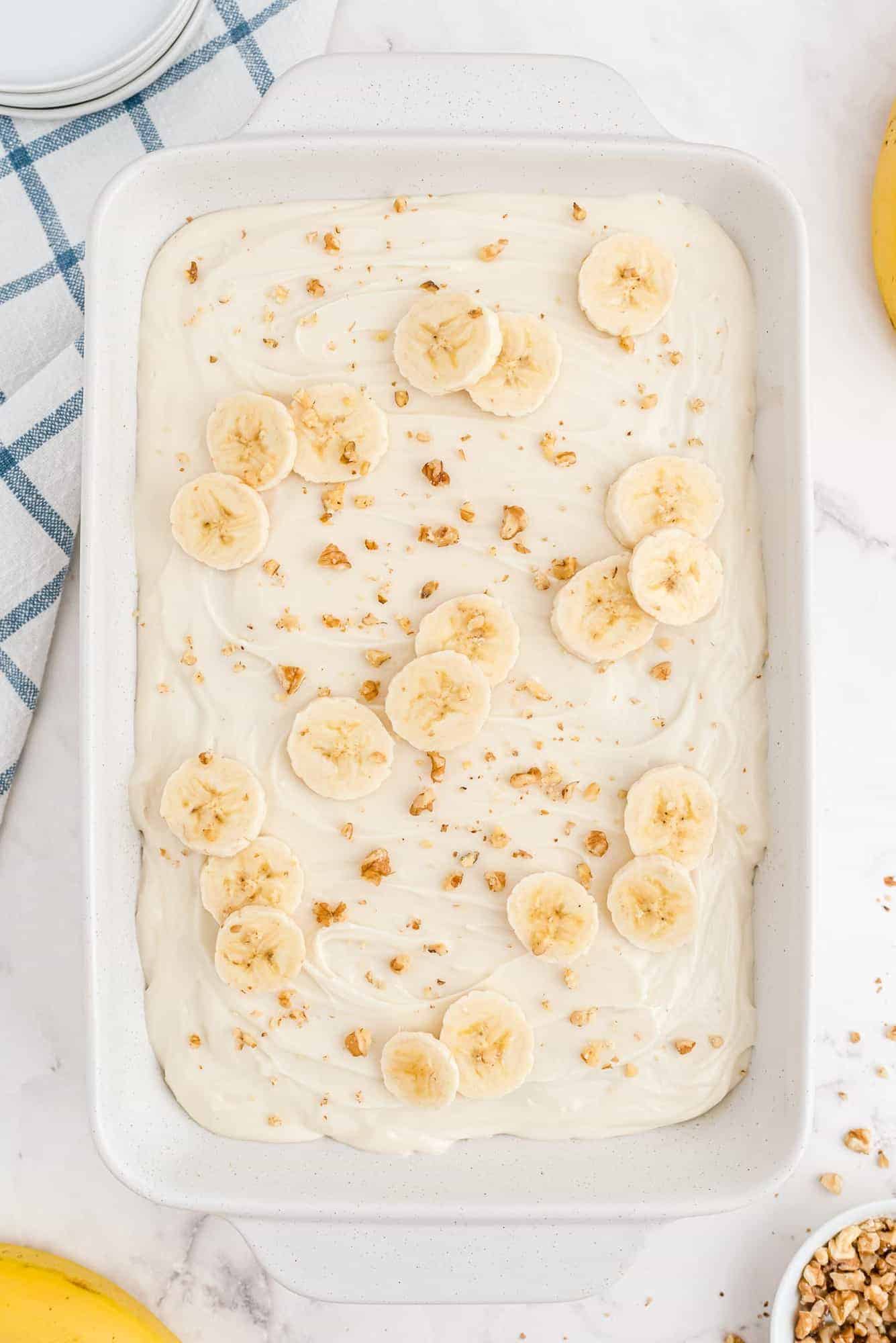 Overhead view of a cake topped with cream cheese frosting, sliced bananas, and chopped walnuts.