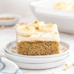 Banana cake with white cream cheese frosting, topped with bananas and nuts.