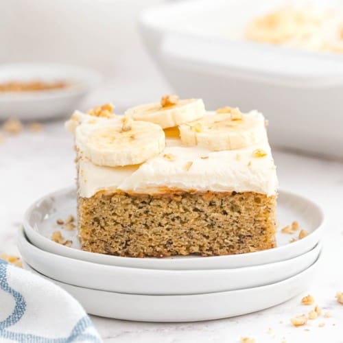 Banana cake with white cream cheese frosting, topped with bananas and nuts.