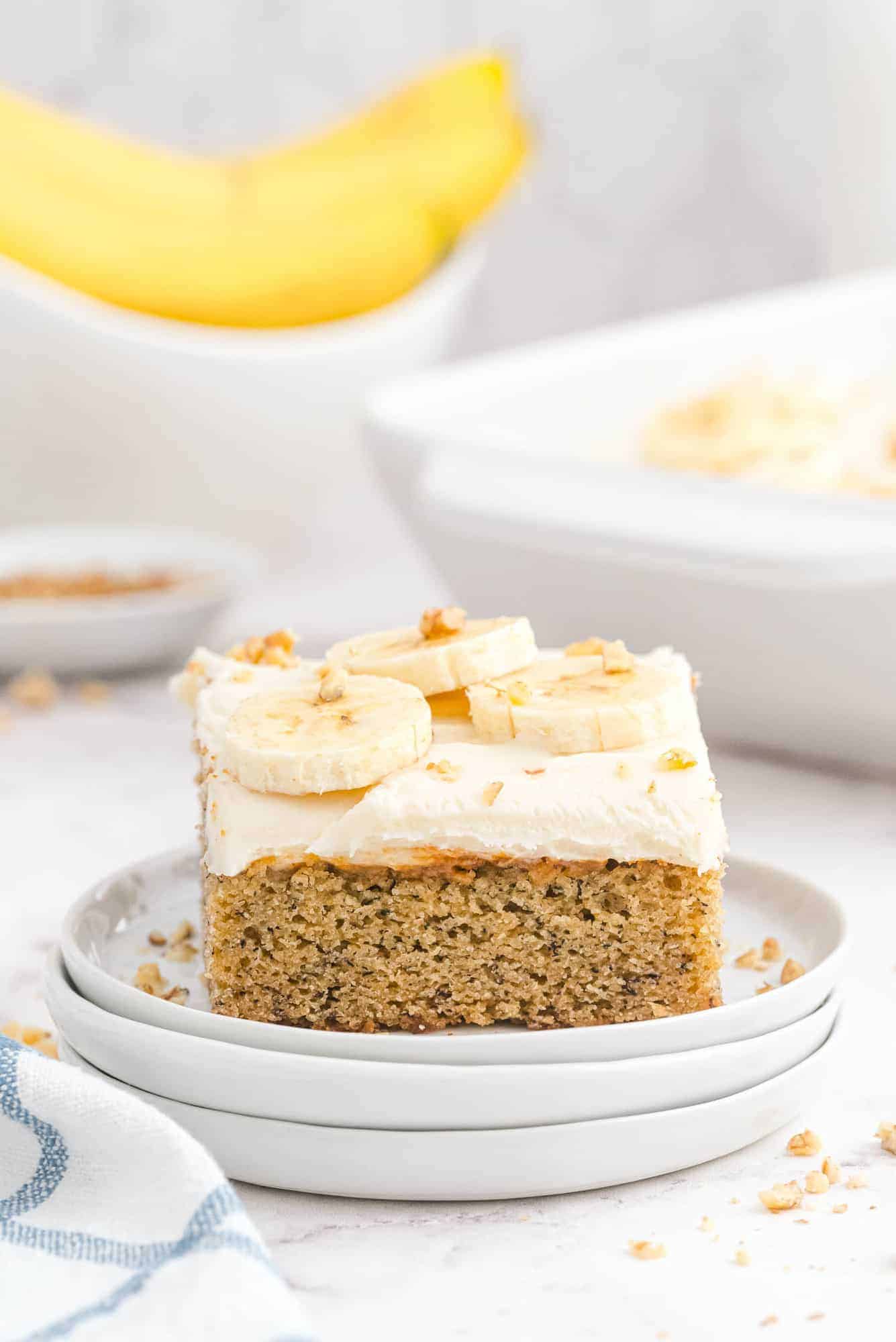 Slice of cake on a plate, bananas in background.